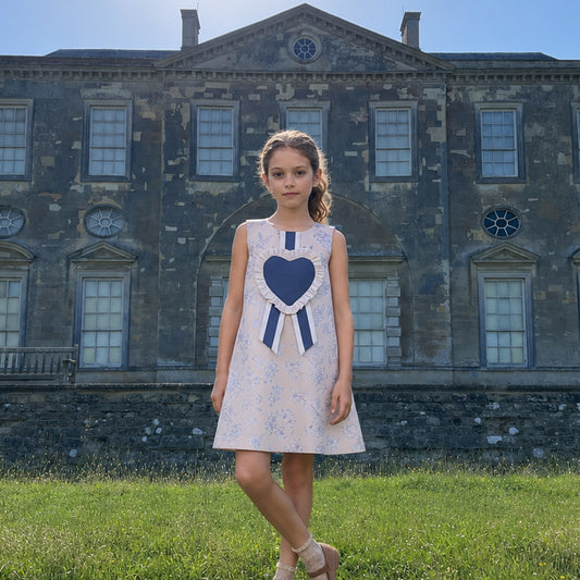 Girls sleeveless floral shift dress with navy heart bib and striped ribbon at collar.