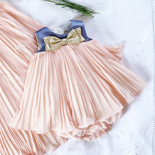 Pink pleated trapeze dress with blue yoke and gold bow; matching ruffled bloomers