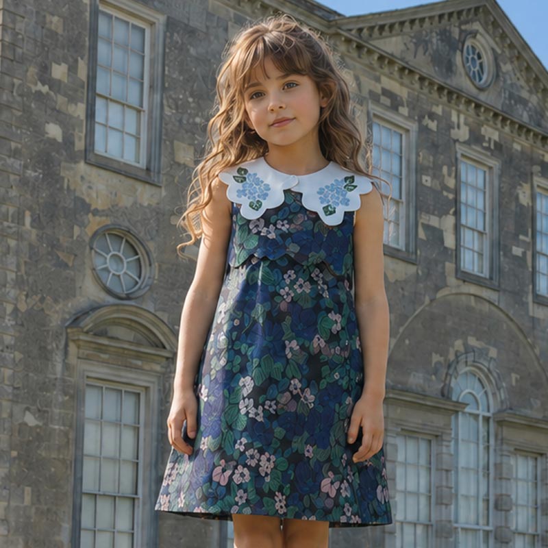 Girl wearing blue floral jacquard dress standing in front of a grand house.