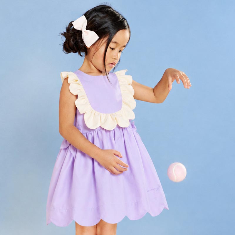 Firls playing with a pink tennis ball and wearing a lilac dress and pink hairclip