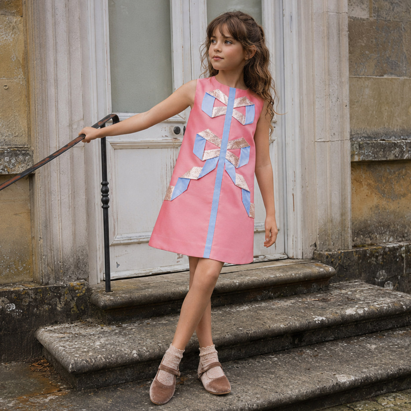 Sleeveless pink shift dress with gold and light-blue ribbon appliques on the bodice.
