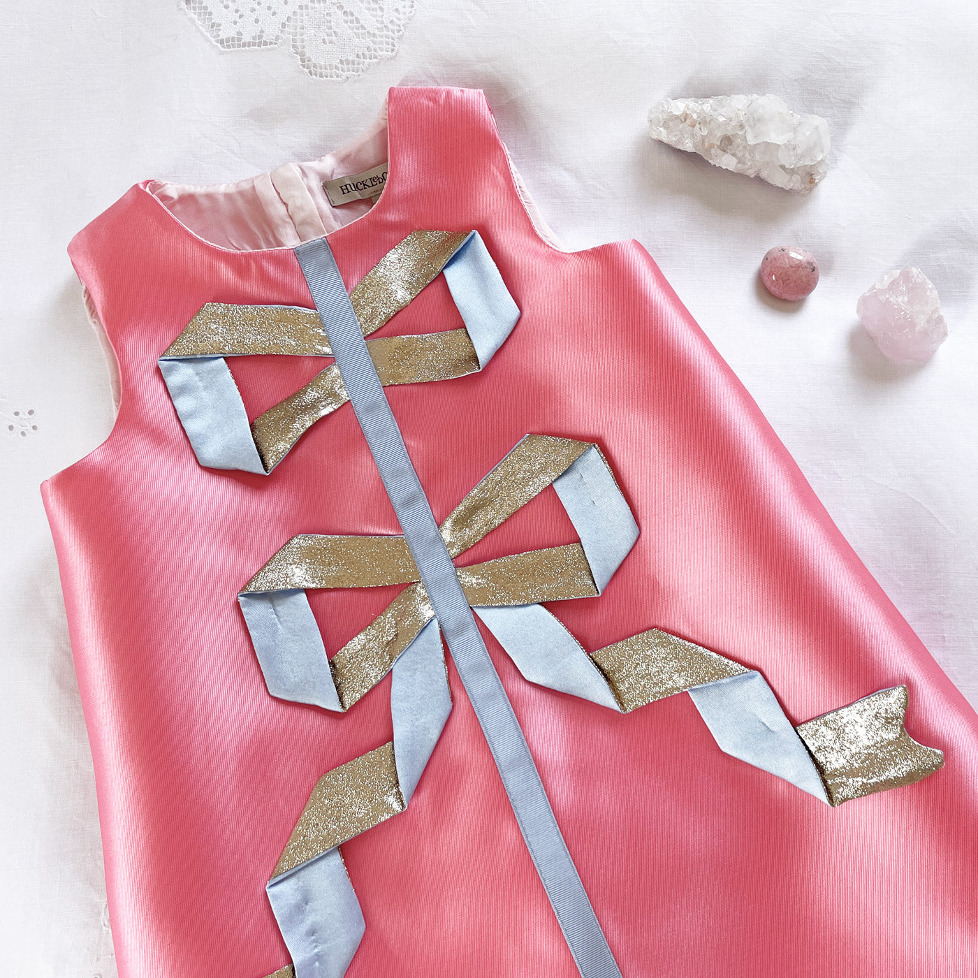 Pink satin shift dress with gold and light-blue ribbon appliques, sleeveless bow detail.