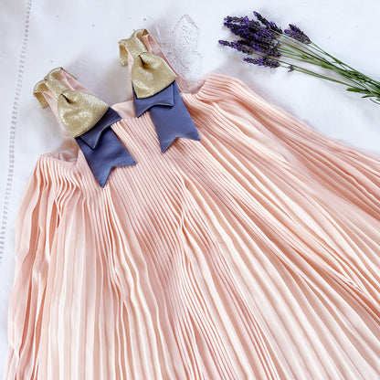 Pleated trapeze dress with peach pleated skirt, navy bodice, and gold bow accents