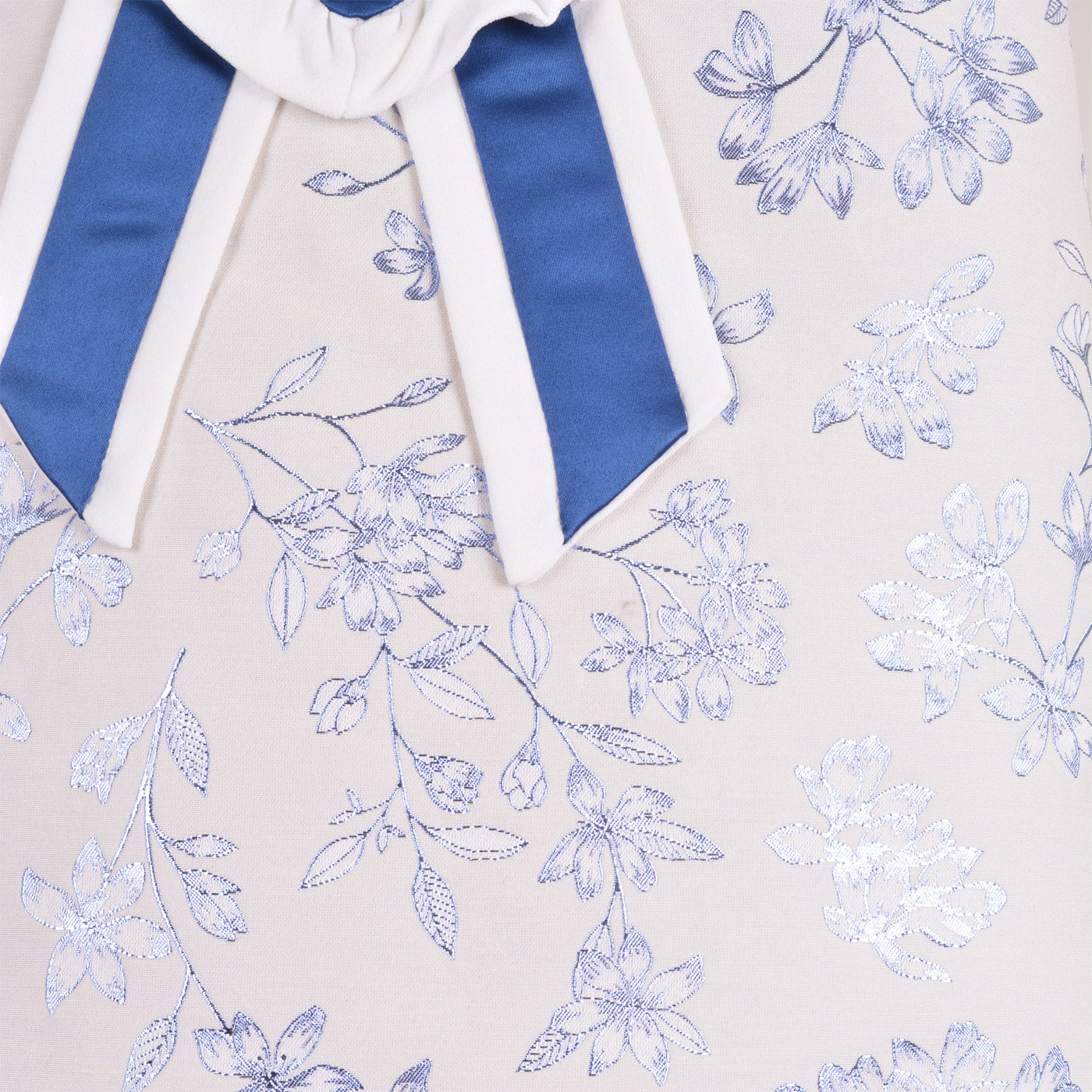 Sleeveless bodice close-up with blue ribbon bow and floral pattern on cream fabric.