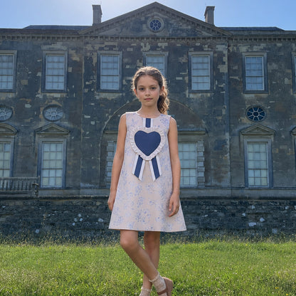 Girls sleeveless floral shift dress with navy heart bib and striped ribbon at collar.