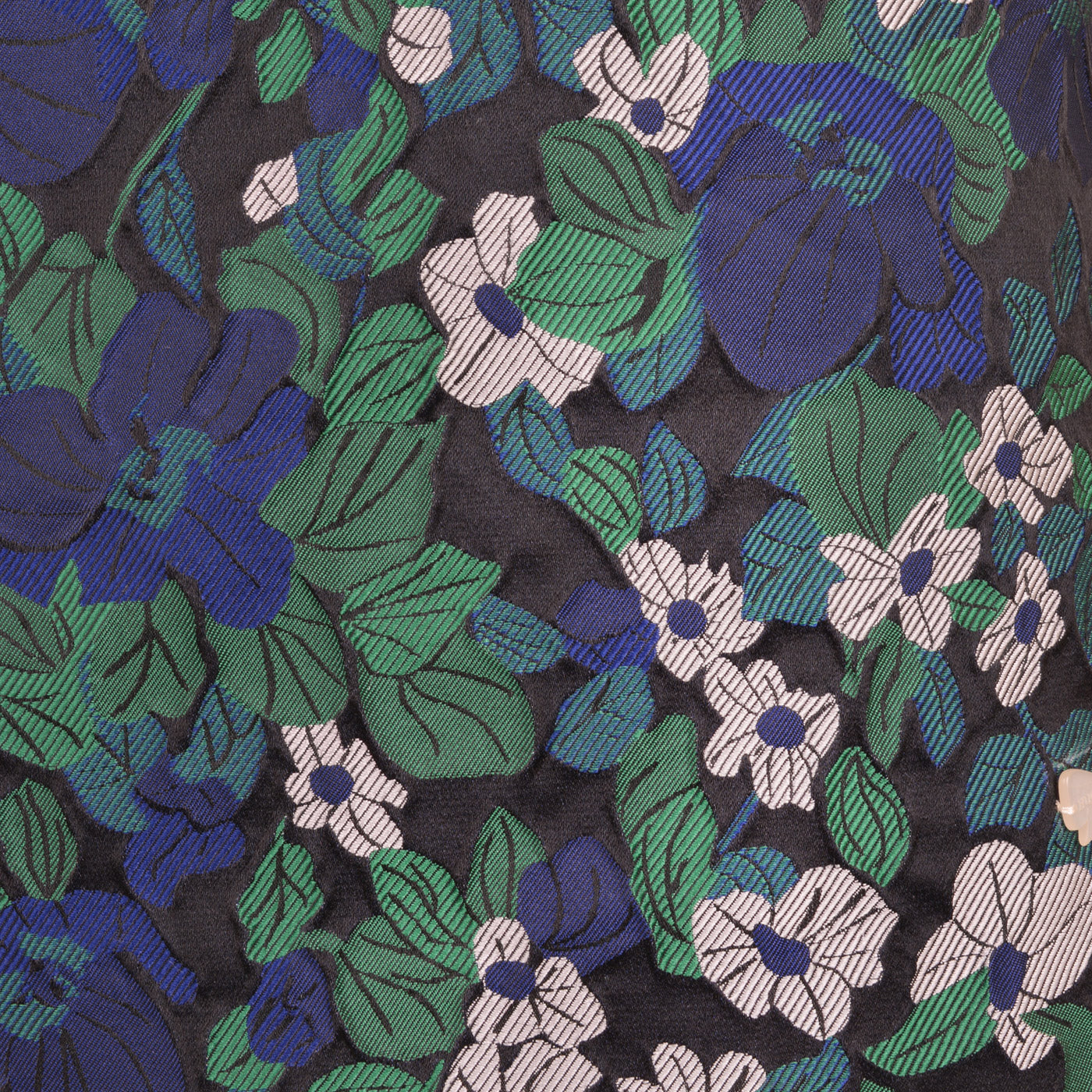 Close-up floral fabric of shift dress with blue flowers, green leaves, and dark purple base