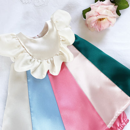 White baby dress with rainbow panels, ruffled bib, and satin skirt hem