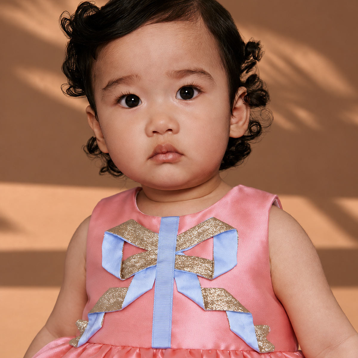 Pink sleeveless shift dress with large gold-and-blue bow detail on the front